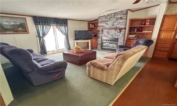 Living room featuring a stone fireplace, vaulted ceiling, a textured ceiling, and carpet flooring