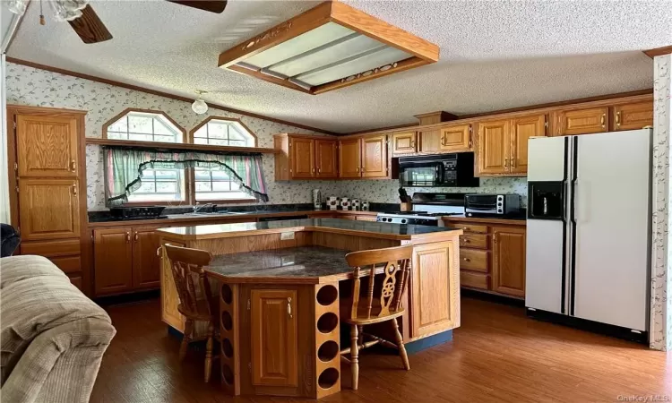 Kitchen featuring white fridge with ice dispenser, wood-type flooring, a kitchen island, and ceiling fan