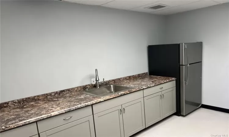 Kitchen featuring sink, stainless steel fridge, a paneled ceiling, and dark stone countertops