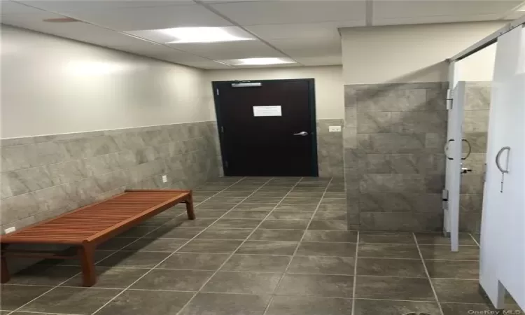 Hallway with dark tile floors, tile walls, and a drop ceiling