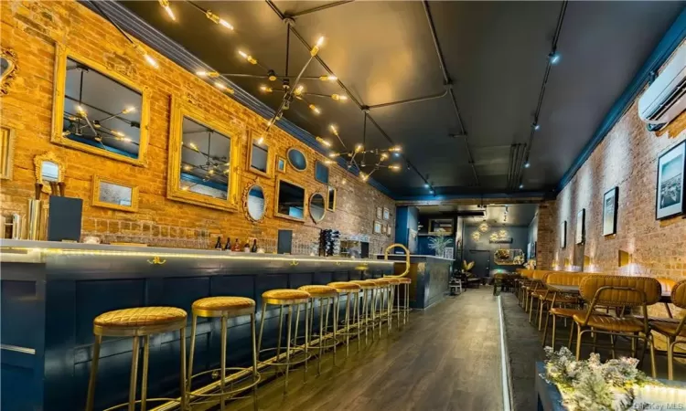 Bar featuring an AC wall unit, dark wood-type flooring, track lighting, and brick wall