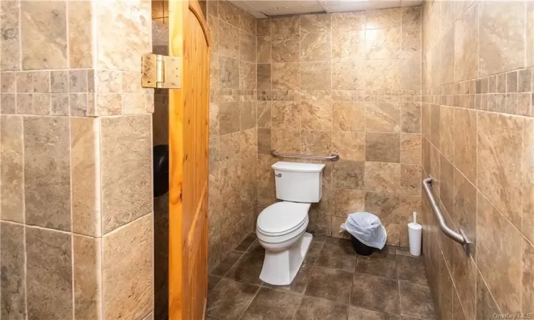 Bathroom featuring toilet, tile patterned flooring, and tile walls