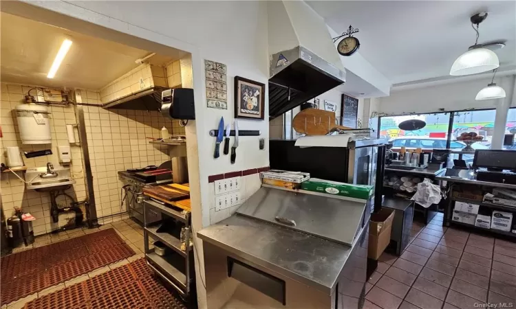 Kitchen with stainless steel counters, tile patterned flooring, tile walls, sink, and decorative light fixtures