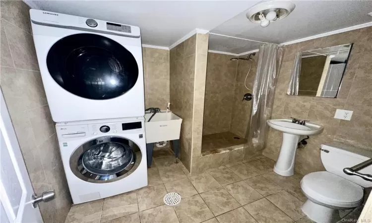 Lower Level - Full bathroom with Clothes washing area and slop sink, with ornamental molding, sink, tile walls, and stacked washer / drying machine