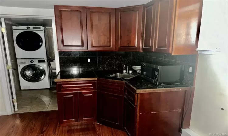 Lower Level - Kitchen with dark hardwood / wood-style flooring, sink, tasteful backsplash, and stacked washing maching and dryer in the full bathroom.