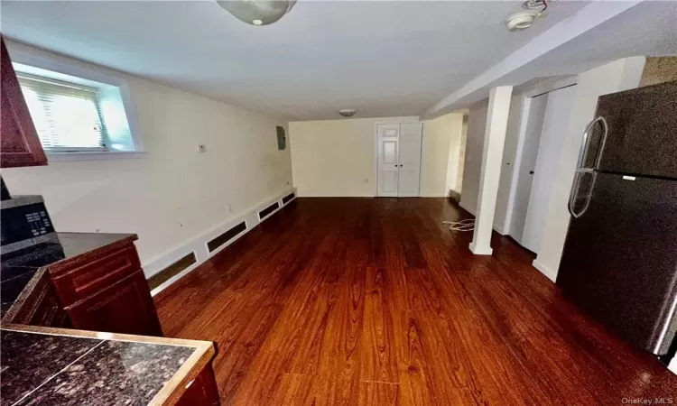 Lower level open concept Kitchen in an empty room featuring stainless fridge and dark hardwood / wood-style flooring