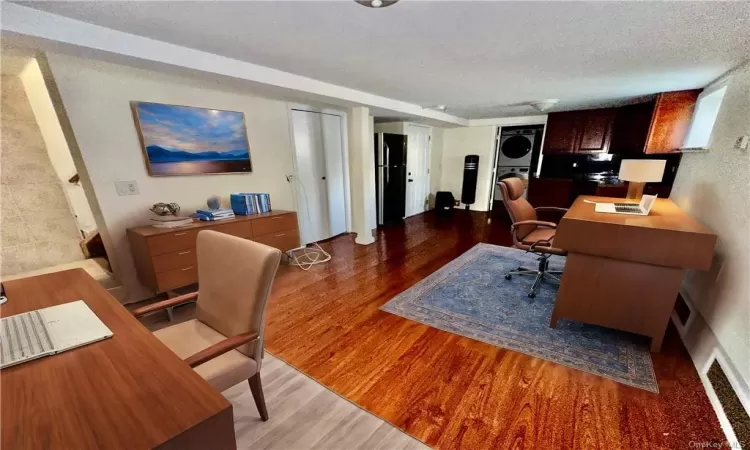 Virtually Staged Lower Level - Staged as a Home office with open concept kitchen and full bathroom with stacked washer / dryer, wood-type flooring, and a textured ceiling