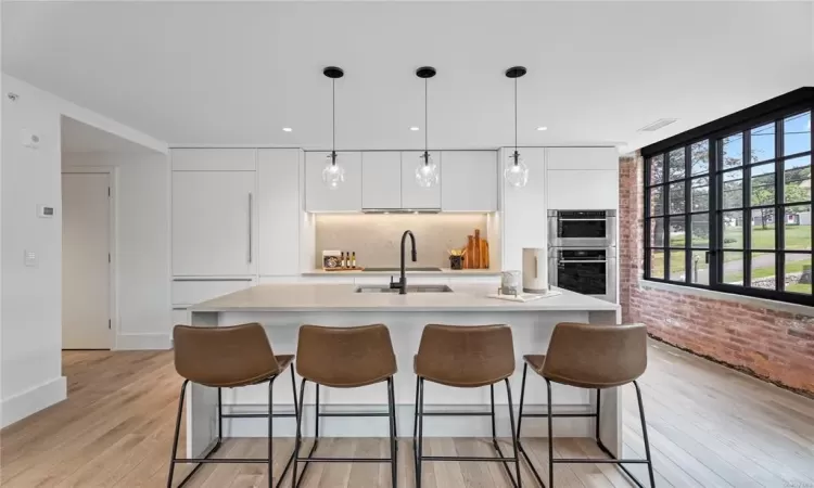 Kitchen featuring white cabinets, sink, light hardwood / wood-style flooring, decorative light fixtures, and stainless steel double oven