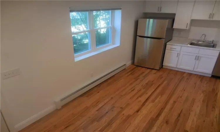 Kitchen featuring white cabinets, sink, stainless steel refrigerator, light wood-type flooring, and baseboard heating