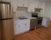 Kitchen with stainless steel appliances, white cabinets, light wood-type flooring, sink, and light stone countertops