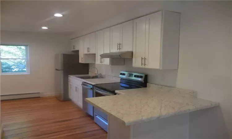 Kitchen featuring white cabinets, baseboard heating, appliances with stainless steel finishes, hardwood / wood-style flooring, and sink