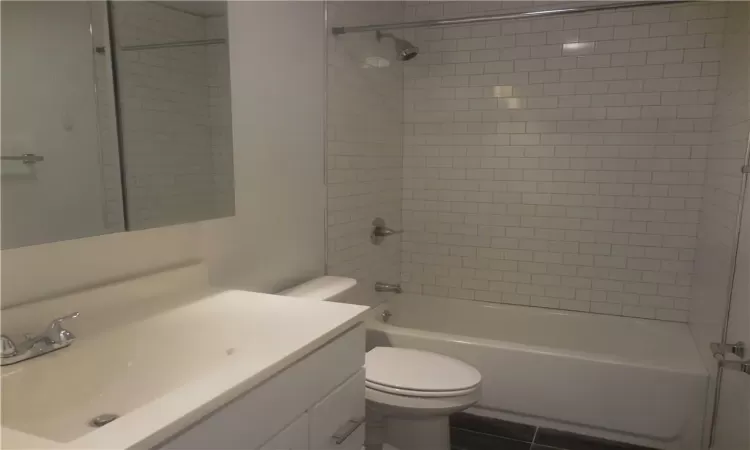 Full bathroom with vanity, tiled shower / bath combo, toilet, and tile patterned floors