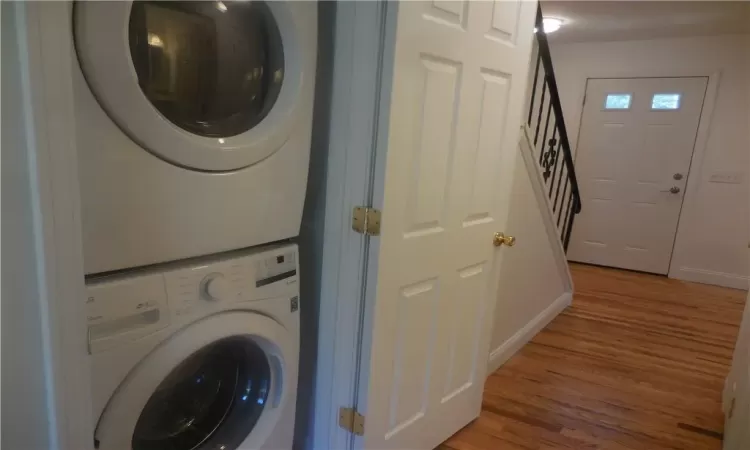 Laundry area with stacked washer and dryer and wood-type flooring