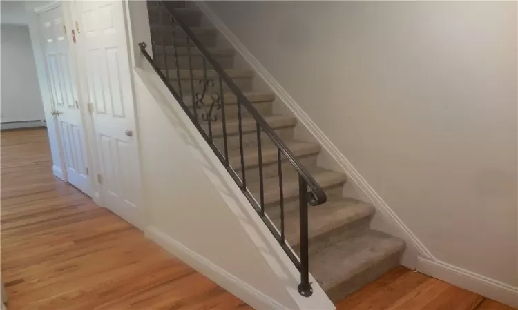 Stairs featuring baseboard heating and light hardwood / wood-style flooring