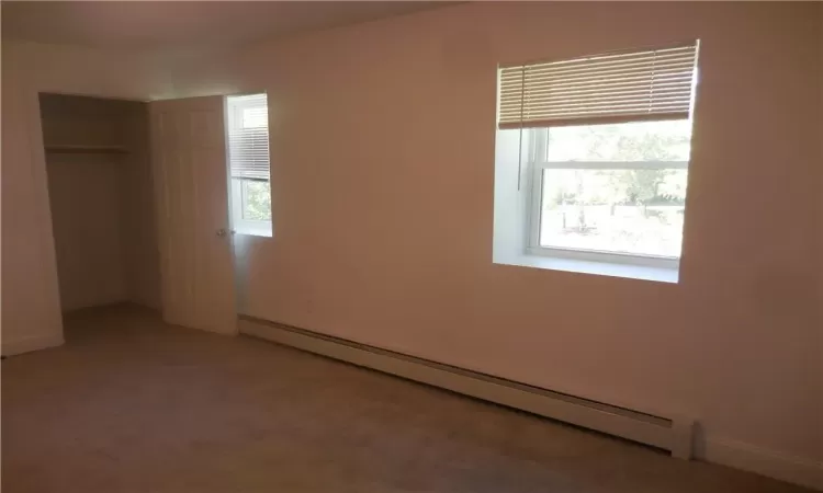 Unfurnished bedroom featuring carpet floors, baseboard heating, and a closet