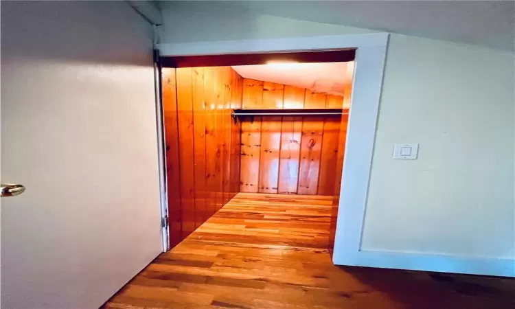 Corridor with wooden walls, vaulted ceiling, and hardwood / wood-style flooring