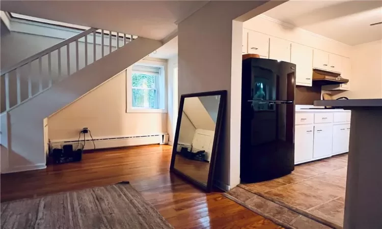 Kitchen featuring hardwood / wood-style flooring, white cabinets, baseboard heating, ornamental molding, and black refrigerator