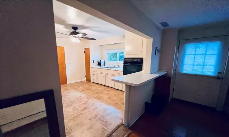 Kitchen featuring white cabinets, kitchen peninsula, black oven, ceiling fan, and sink