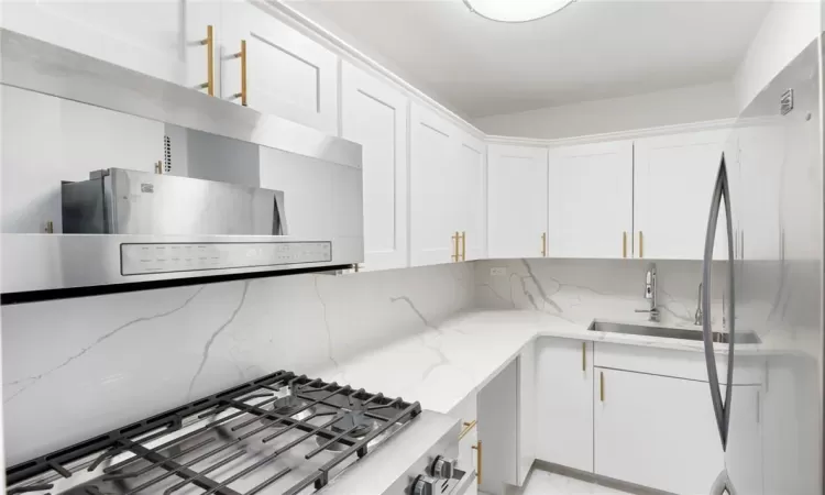 Kitchen featuring light stone countertops, sink, appliances with stainless steel finishes, and white cabinetry