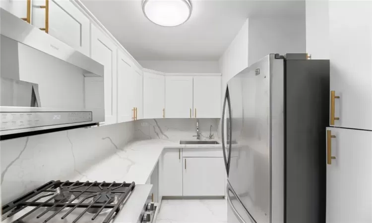 Kitchen featuring sink, light stone countertops, stainless steel appliances, and white cabinets