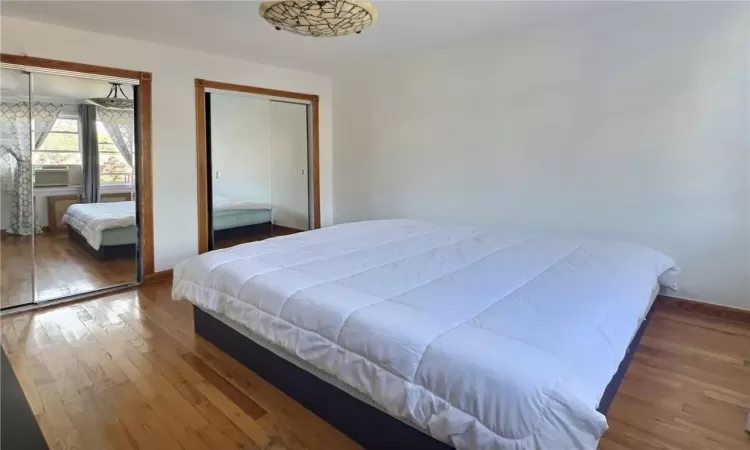 Bedroom featuring hardwood / wood-style flooring, cooling unit, and multiple closets