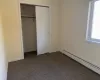 Unfurnished bedroom featuring a closet, a baseboard heating unit, and dark carpet