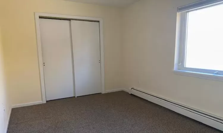 Unfurnished bedroom featuring a closet, a baseboard heating unit, and dark carpet