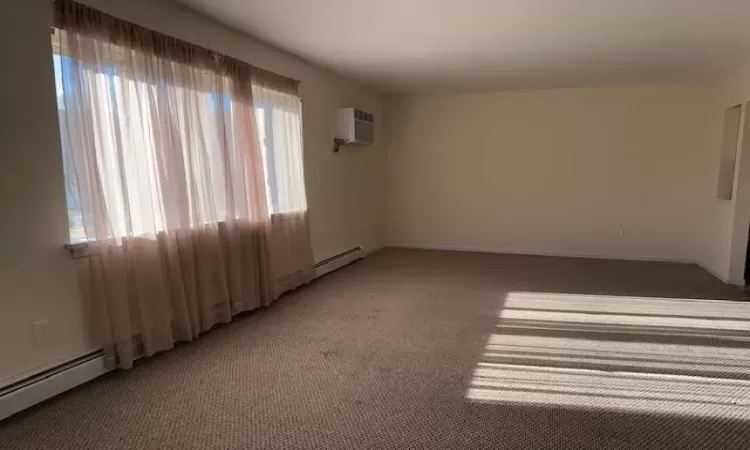 Carpeted spare room featuring a wall unit AC and baseboard heating