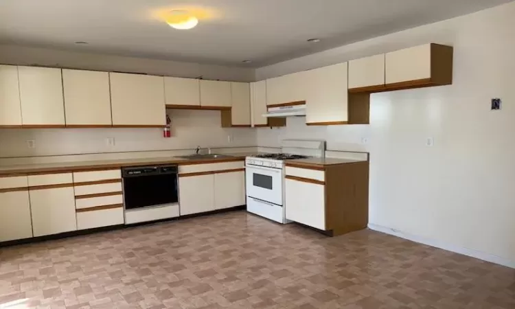 Kitchen featuring black dishwasher, cream cabinetry, sink, and white gas stove