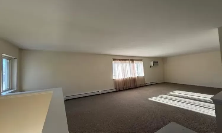 Unfurnished room featuring a baseboard heating unit, a wall mounted air conditioner, and carpet floors