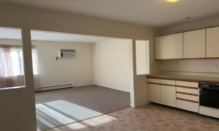 Kitchen with a baseboard heating unit, a wall unit AC, black dishwasher, light carpet, and cream cabinetry