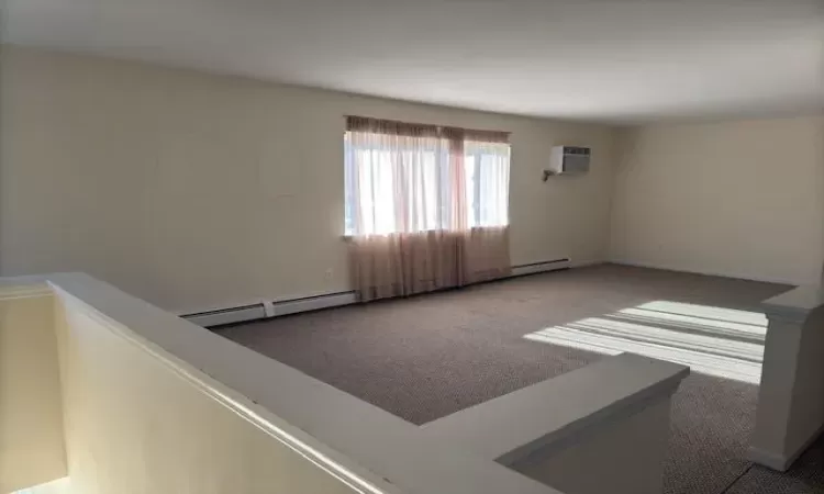 Carpeted empty room featuring a wall mounted air conditioner and a baseboard radiator