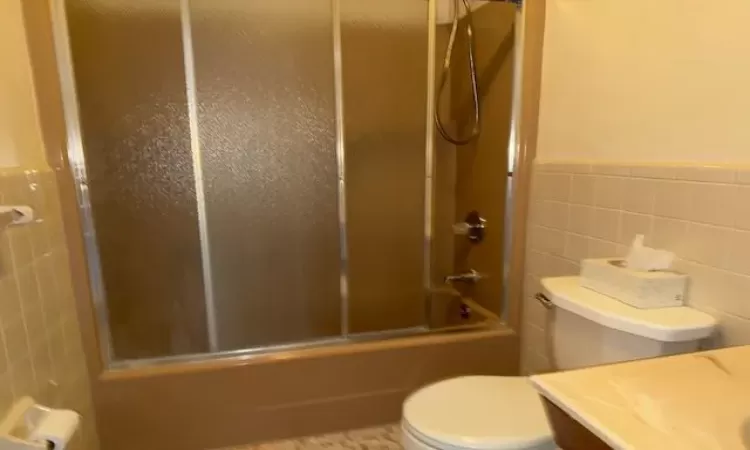 Full bathroom featuring toilet, vanity, tile walls, and enclosed tub / shower combo