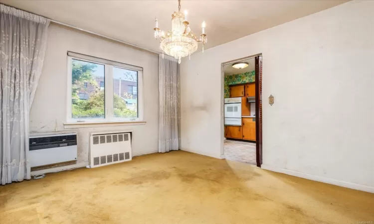 Carpeted empty room featuring radiator heating unit, an inviting chandelier, and a wall unit AC