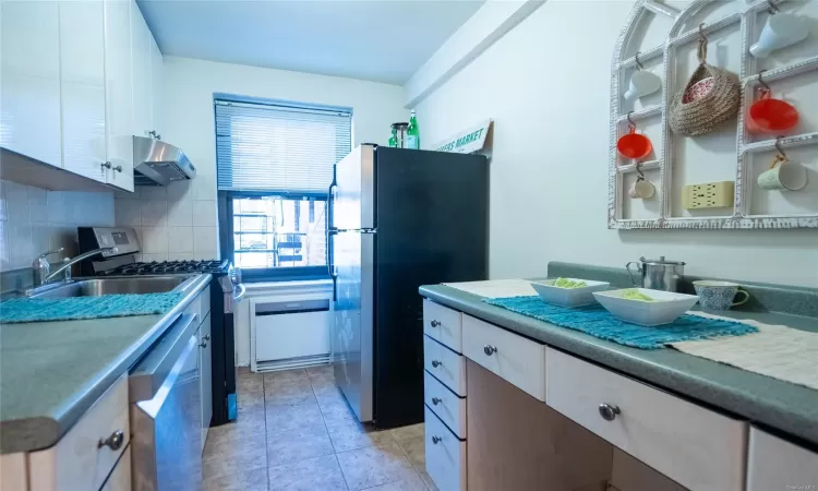 Kitchen with appliances with stainless steel finishes, tasteful backsplash, ventilation hood, sink, and white cabinetry