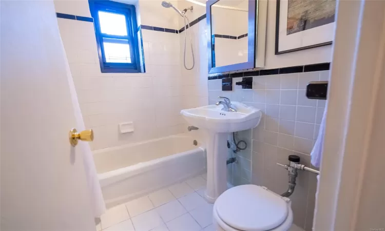 Bathroom with tile patterned flooring, shower / tub combo, tile walls, and toilet