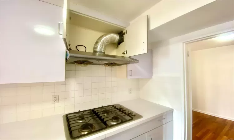 Kitchen with dark hardwood / wood-style floors, white cabinets, gas cooktop, range hood, and tasteful backsplash