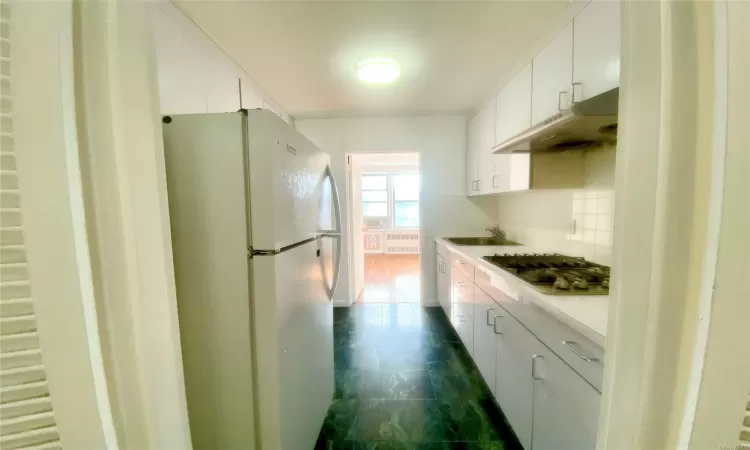 Kitchen with white fridge, stainless steel gas cooktop, radiator, decorative backsplash, and white cabinetry