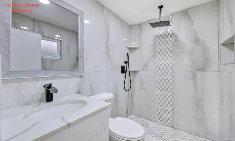 Bathroom featuring tiled shower, toilet, tile walls, and vanity