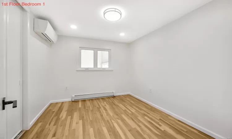 Empty room with a wall mounted AC, light hardwood / wood-style floors, and baseboard heating