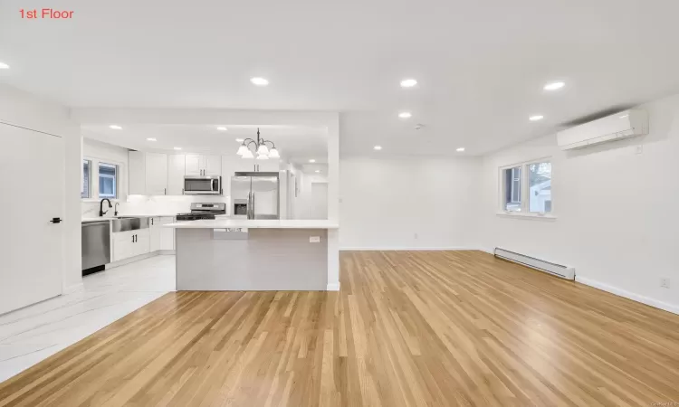 Kitchen with a wall mounted air conditioner, appliances with stainless steel finishes, light wood-type flooring, baseboard heating, and white cabinetry