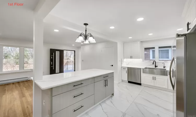 Kitchen with stainless steel appliances, a baseboard heating unit, a chandelier, pendant lighting, and white cabinets