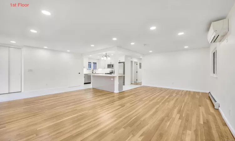 Unfurnished living room featuring sink, a baseboard radiator, an inviting chandelier, a wall mounted AC, and light hardwood / wood-style floors