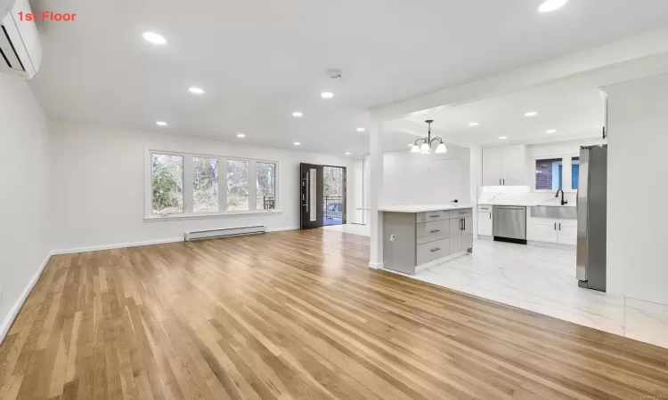 Unfurnished living room with sink, a baseboard radiator, an inviting chandelier, light hardwood / wood-style flooring, and a wall unit AC