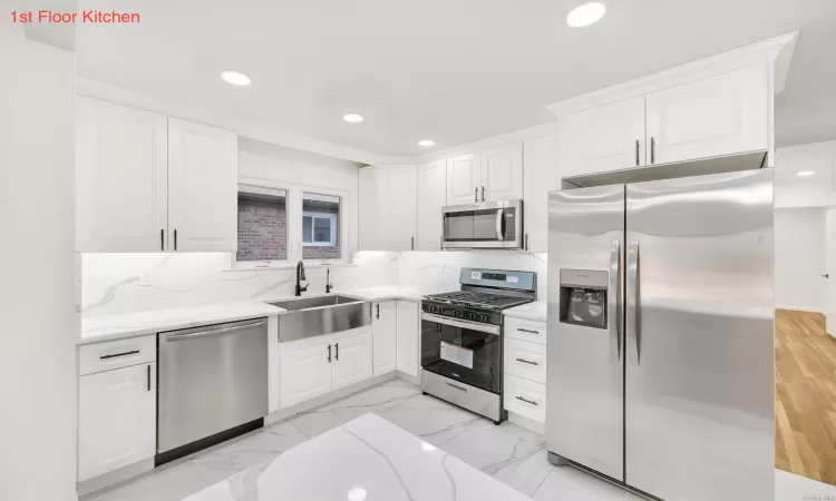 Kitchen with decorative backsplash, sink, white cabinets, and appliances with stainless steel finishes