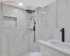 Bathroom with toilet, a tile shower, tile walls, and vanity