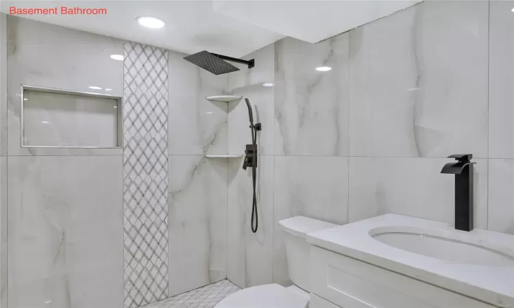 Bathroom with toilet, a tile shower, tile walls, and vanity