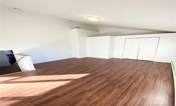 Unfurnished bedroom with a closet, dark hardwood / wood-style flooring, a baseboard radiator, and lofted ceiling