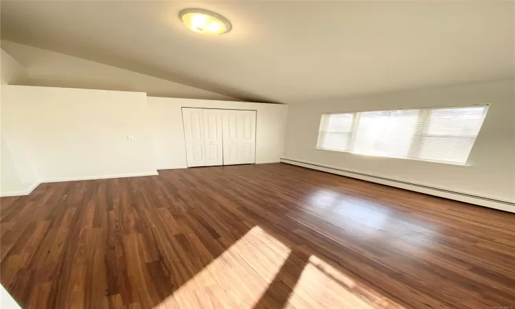 Unfurnished bedroom featuring a closet, dark hardwood / wood-style flooring, lofted ceiling, and a baseboard heating unit