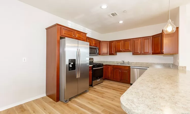 Kitchen with hanging light fixtures, stainless steel appliances, light wood-type flooring, and sink